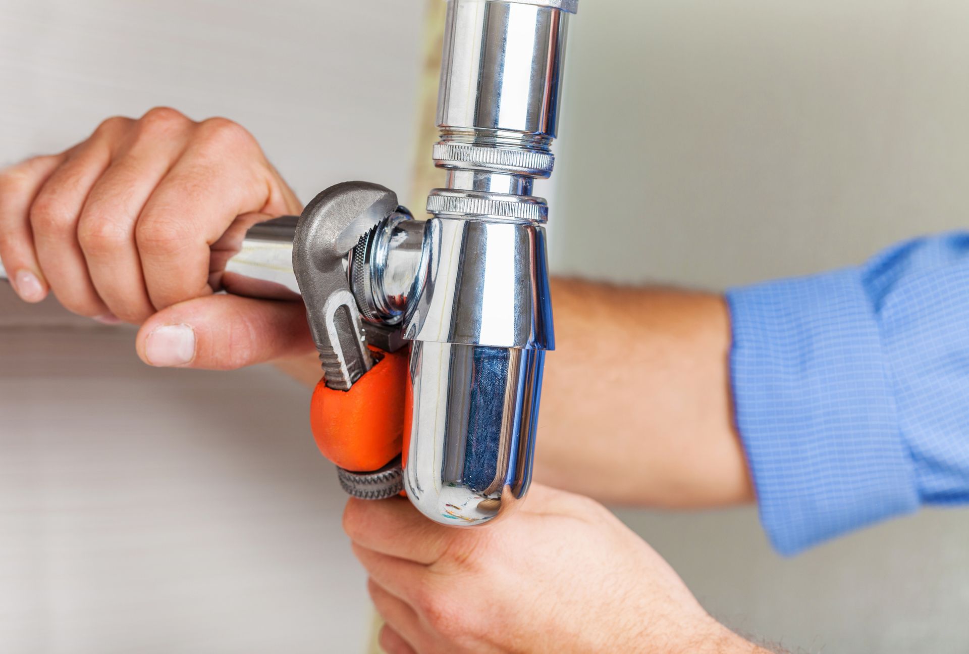 Plumber tightening chrome sink drain pipe with wrench during professional plumbing repair service job.