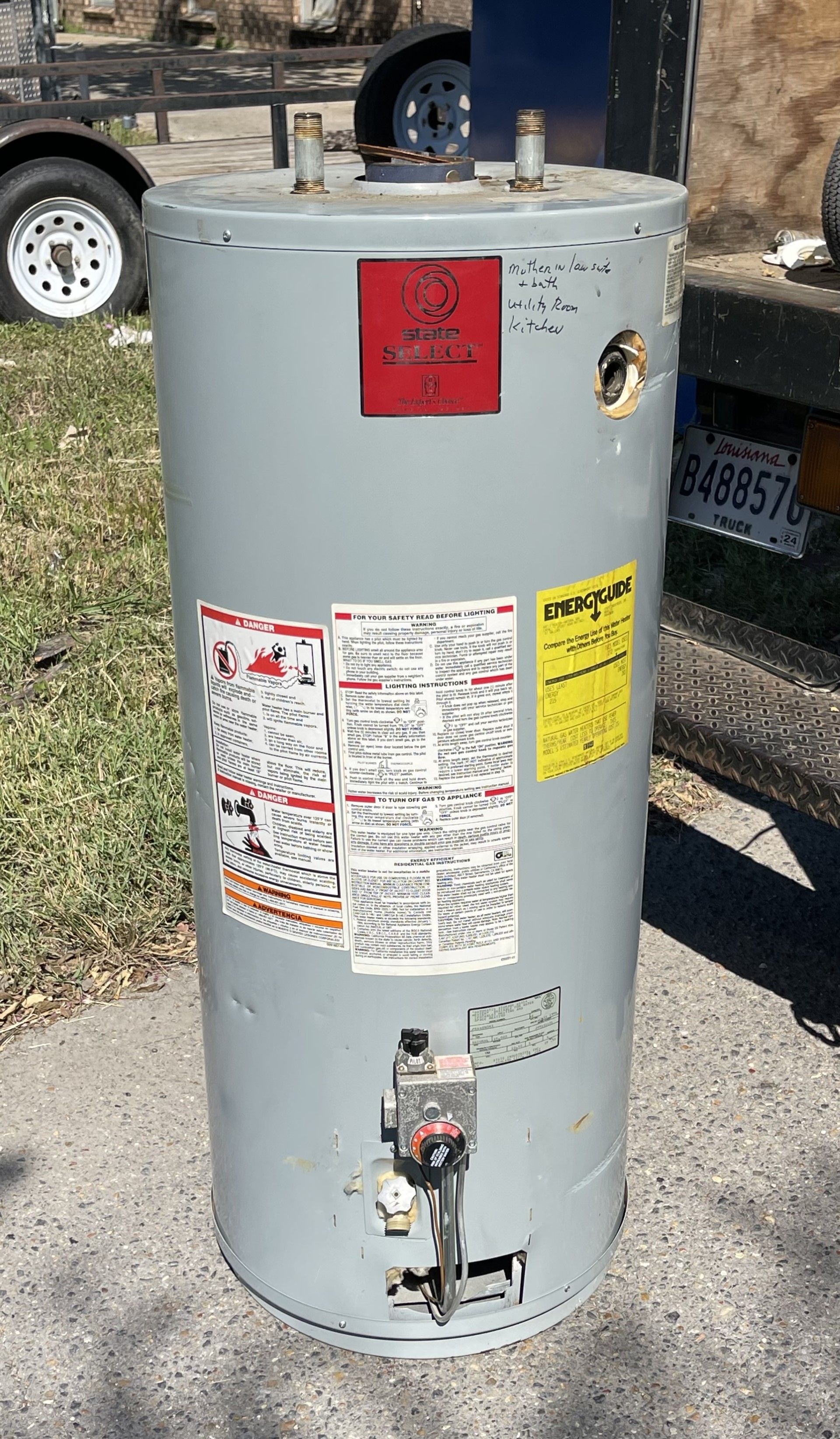 Gray water heater with safety labels in outdoor setting.