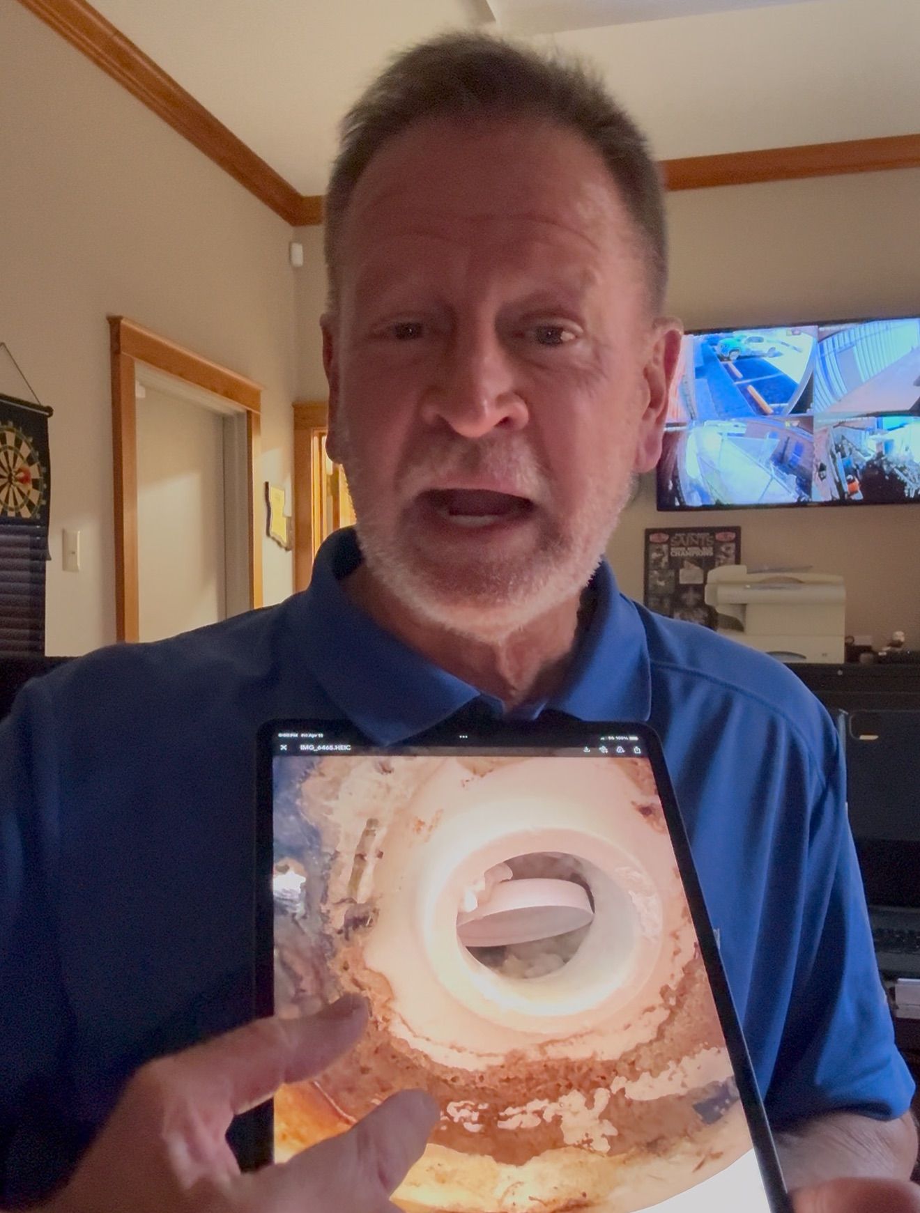 Man in blue shirt holds a tablet displaying an image of a tunnel-like structure, indoors.