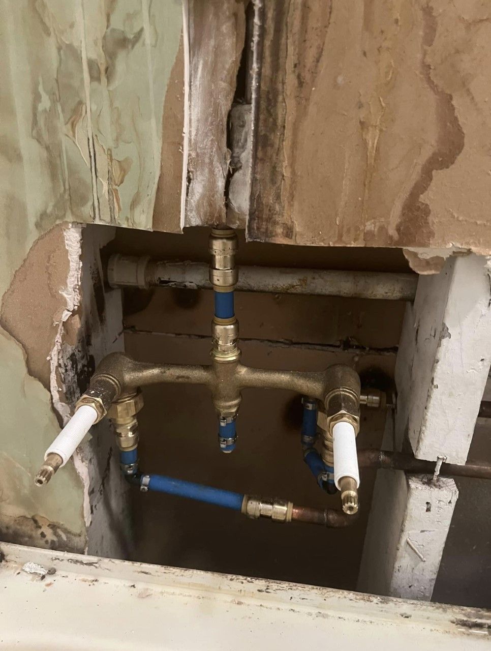 Open wall with exposed plumbing pipes and valves inside a damaged bathroom or utility area