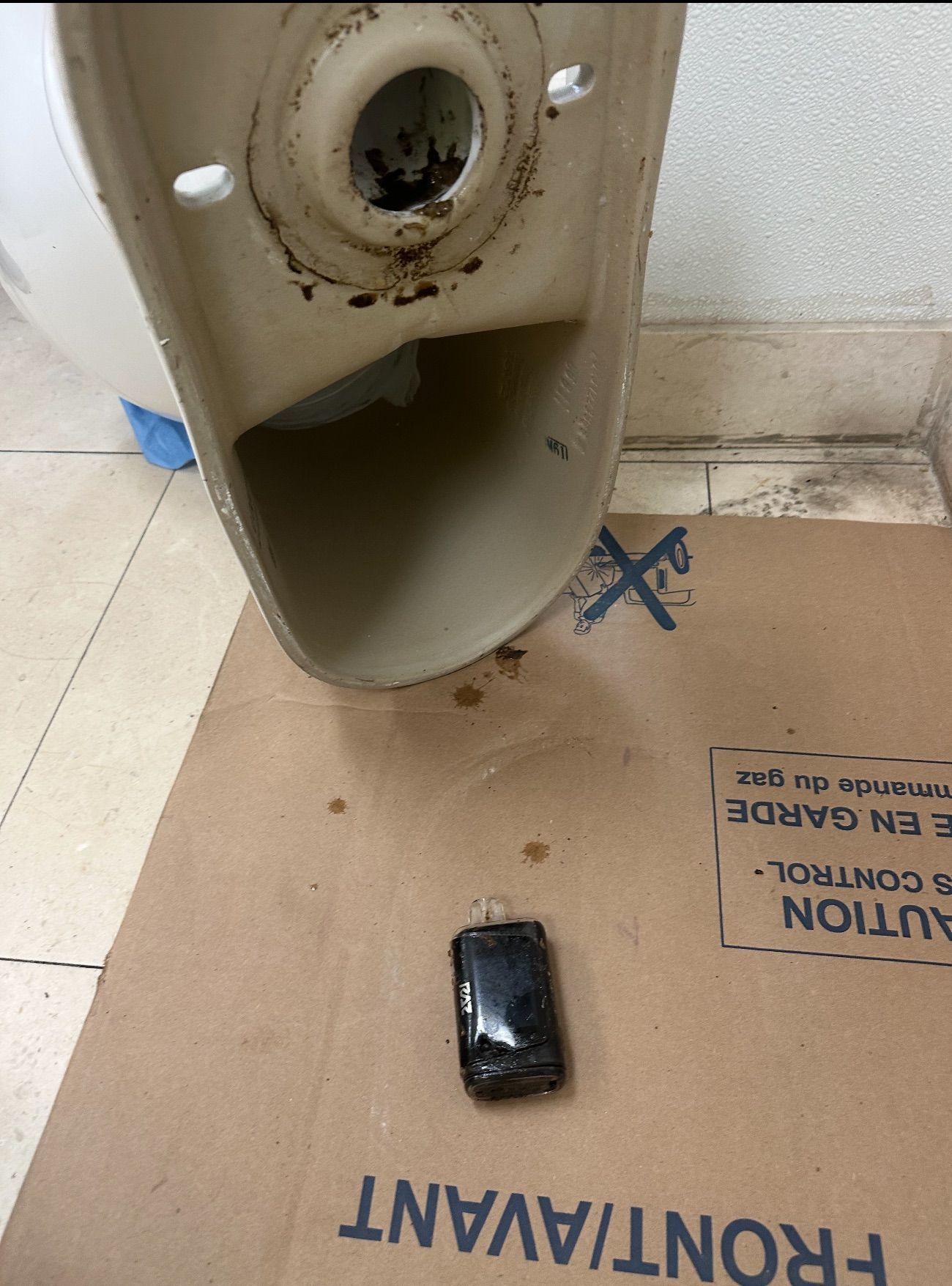 Toilet bowl overturned, with a cell phone at the bottom, resting on cardboard.