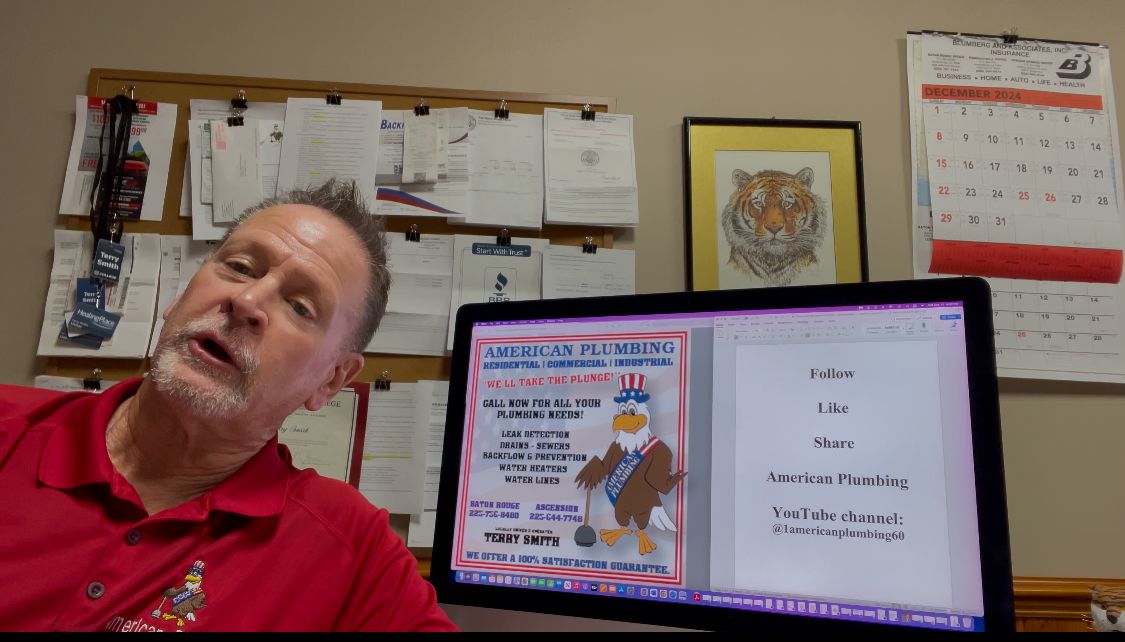 Man in red shirt beside open laptop in office, with wall calendars and notes behind him.