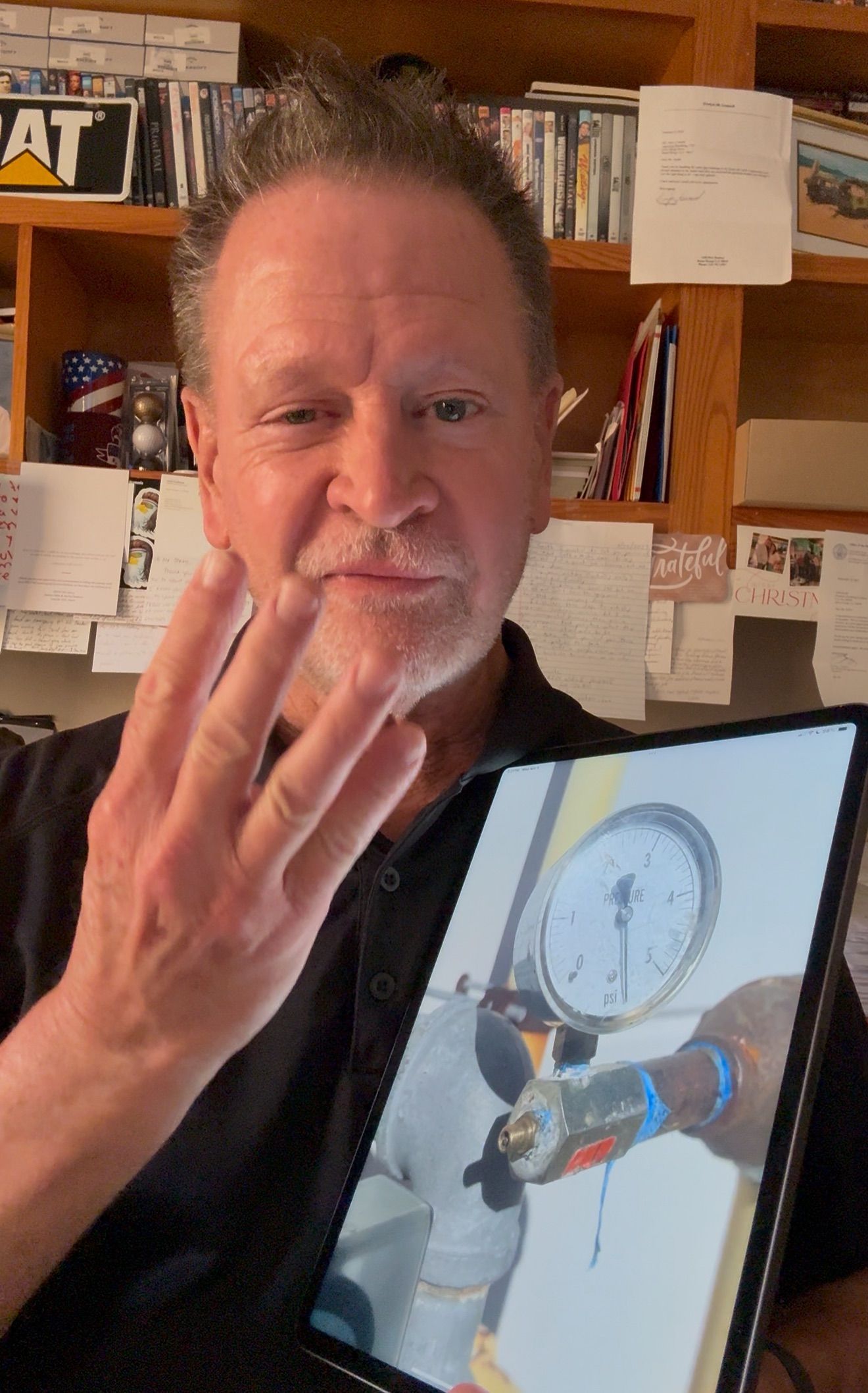 Man holding up three fingers beside a tablet showing a 3D clock-like design in a workshop.
