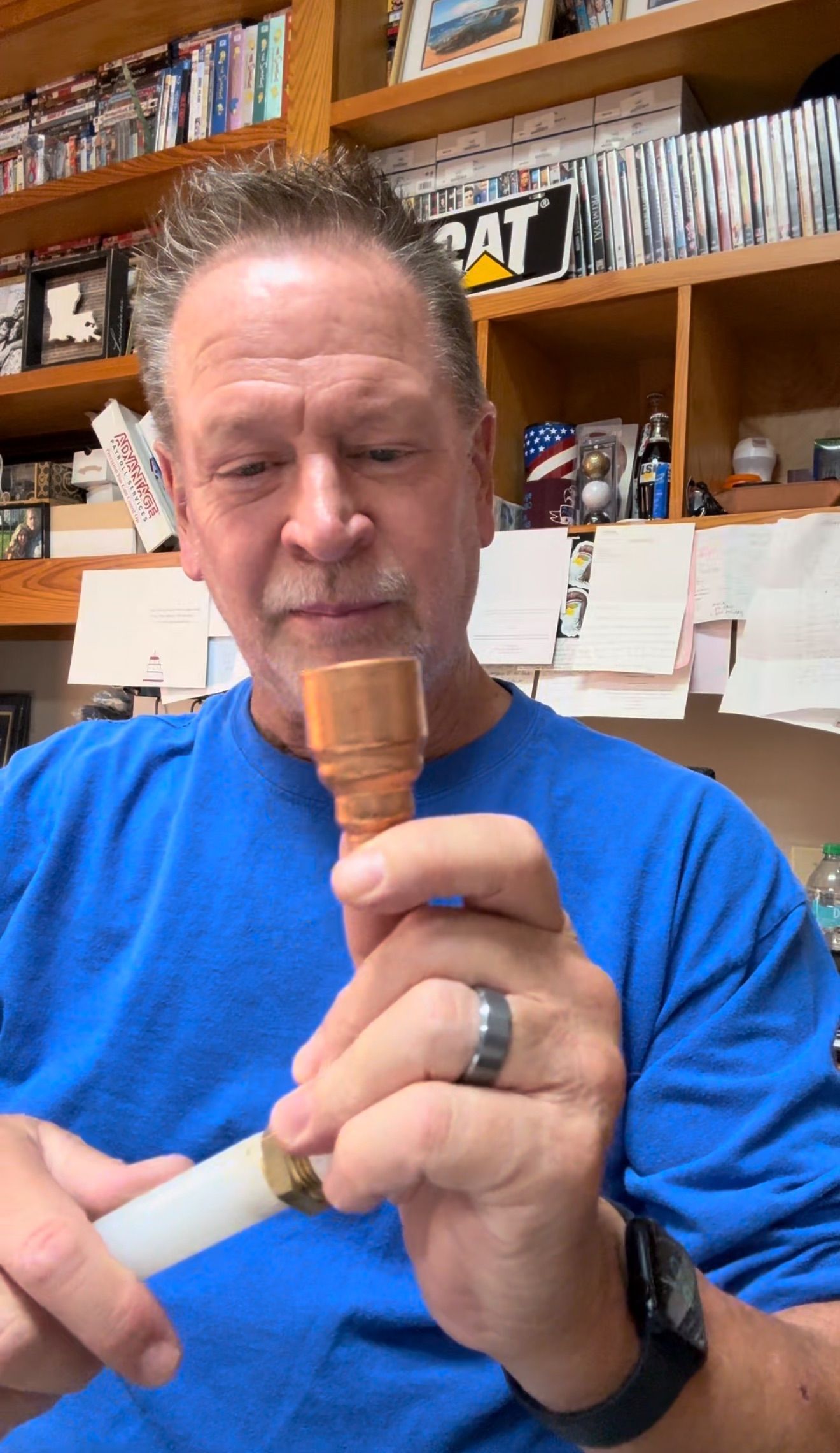 Person in a blue shirt holding a small wooden object in a room with shelves and books behind them.