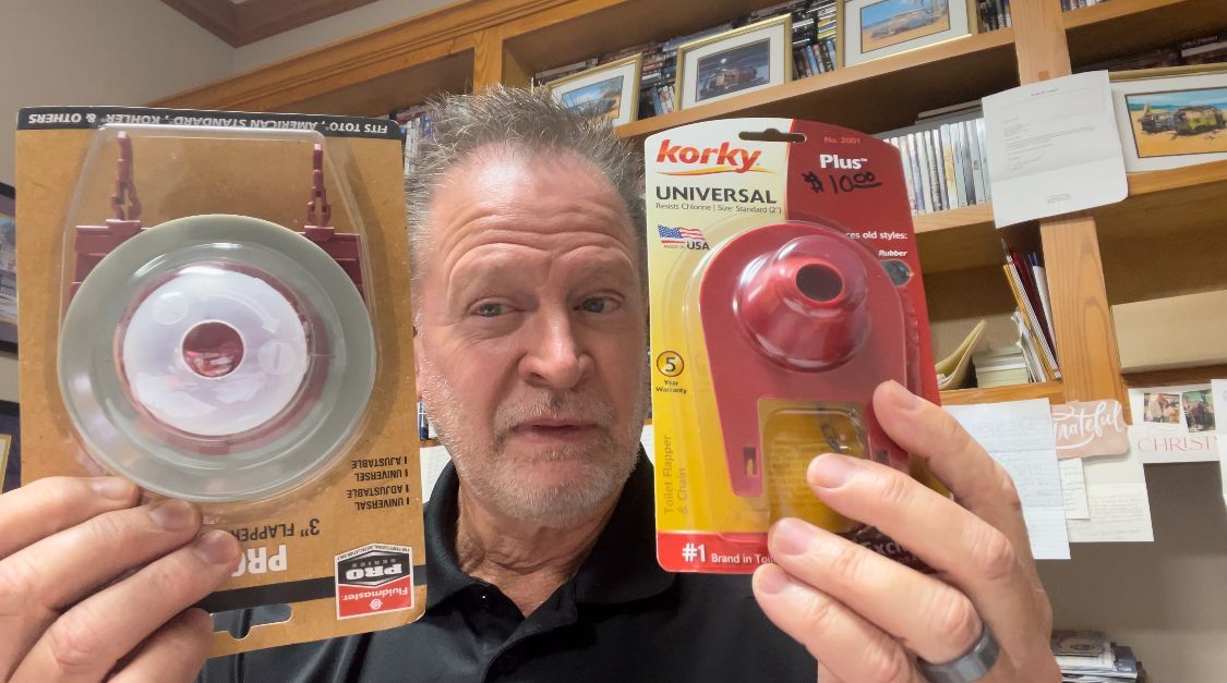 Man in a workshop holding two packaged tape measures, one silver and one red.