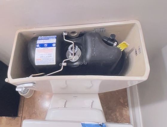 Open toilet tank with black flushing mechanism and labeled water-saving device inside.