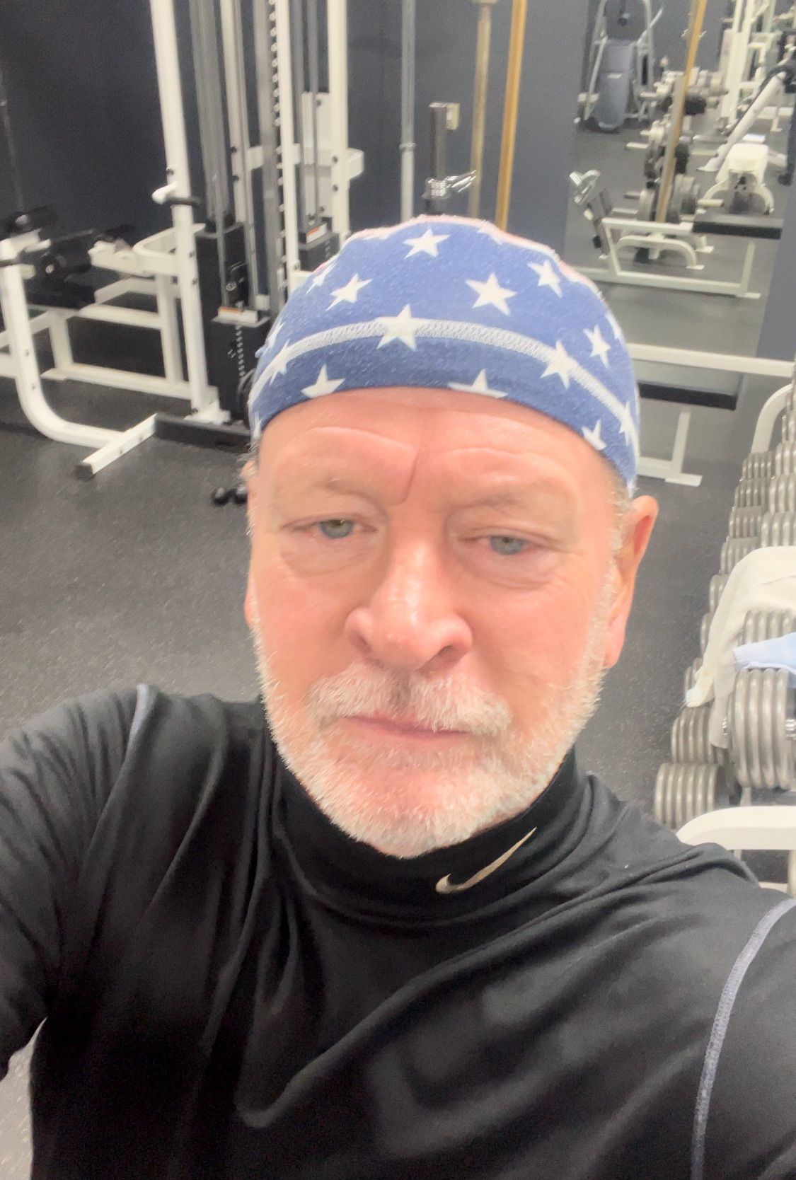Man in blue star-patterned headscarf taking a gym selfie, with weight machines in the background
