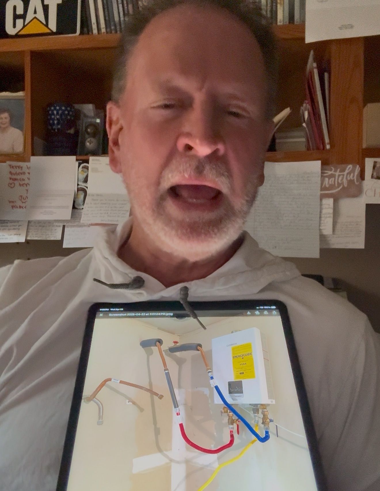Man holding a tablet with a map open, standing indoors in front of shelves and papers.