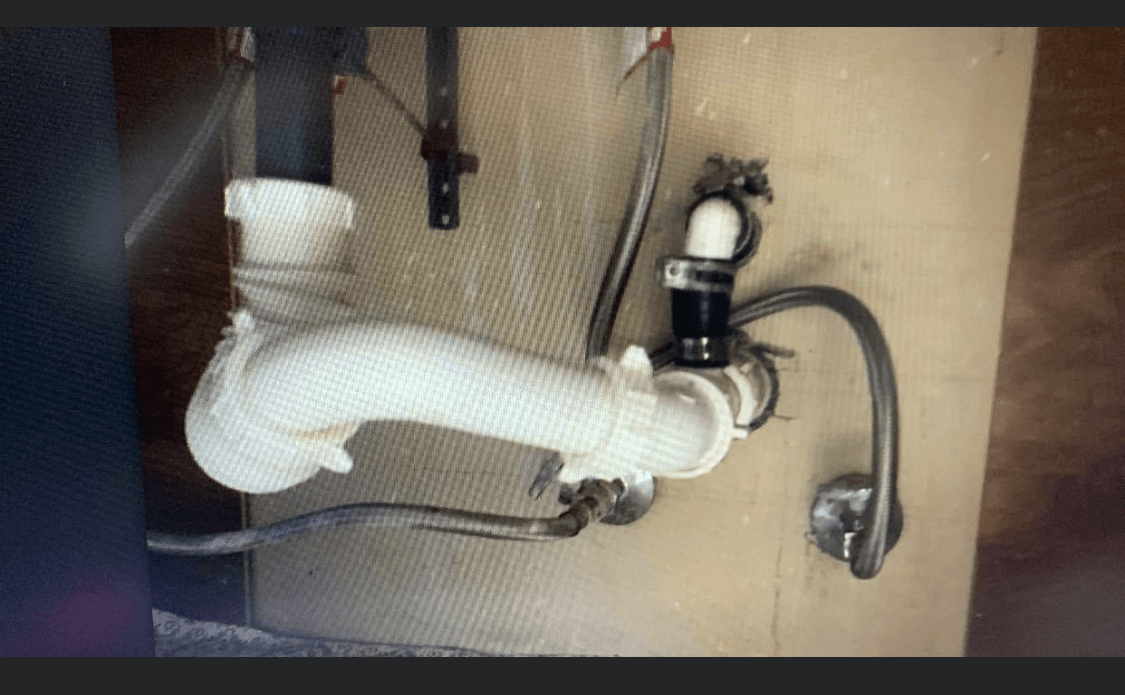 White sink drain pipes and faucet beneath a sink against a beige wall.