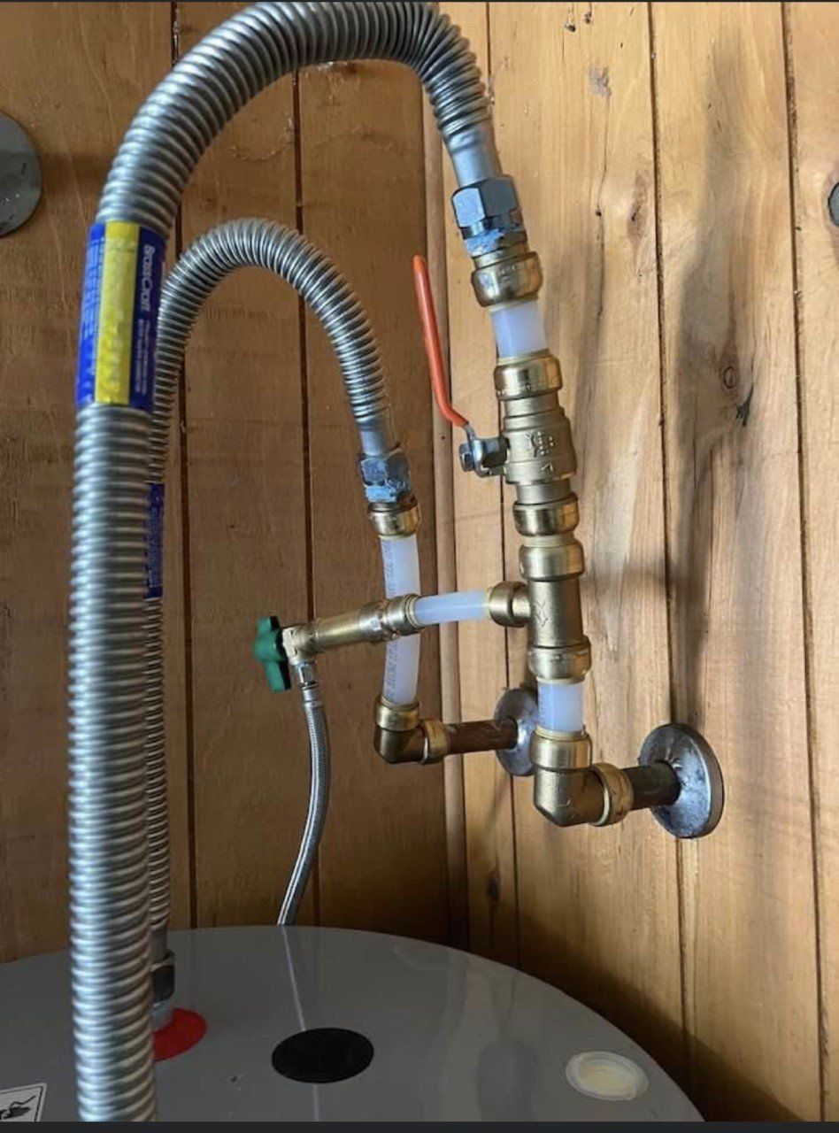 Water heater with connected pipes, valves, and flexible gas line against a wooden wall.
