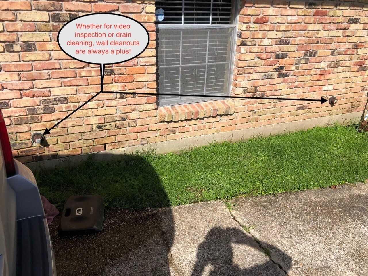 Brick house wall with a window and a speech bubble sign above a grassy strip and driveway shadow