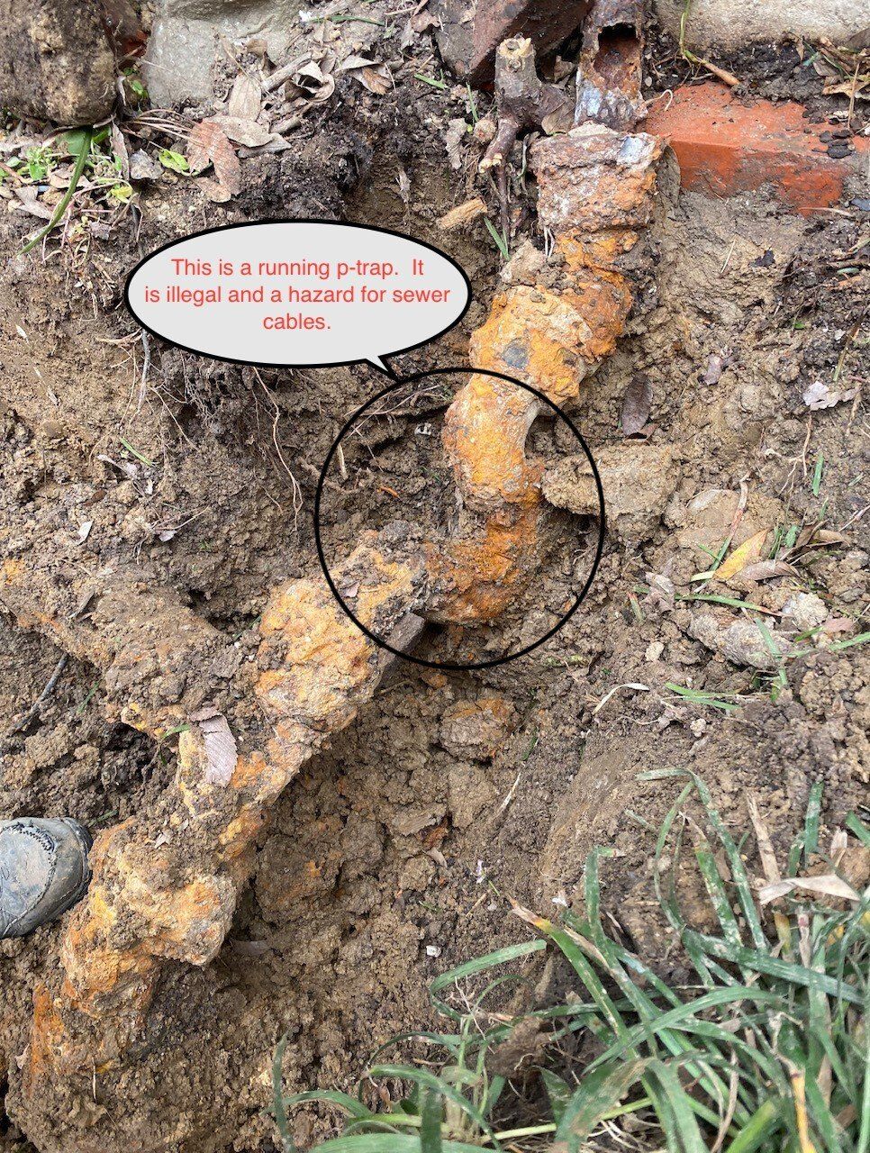 Excavated rusty pipe section in dirt, next to brick wall.