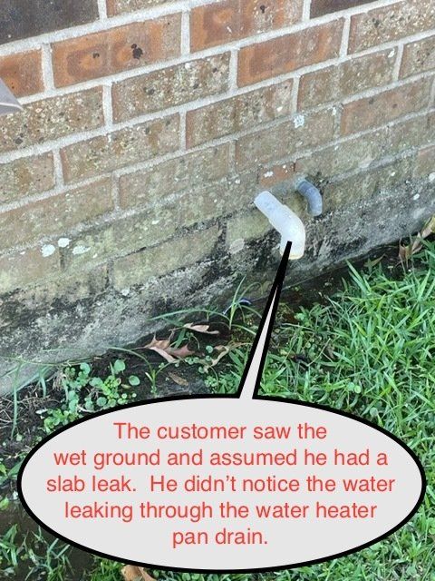 Wet ground by brick wall with a leaking pipe near a water heater drain.