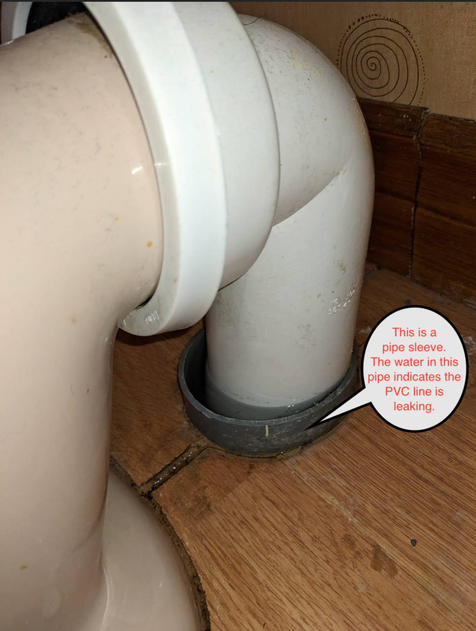 Toilet drain pipe connection, white pipe with a gray base sleeve, on a wooden floor.