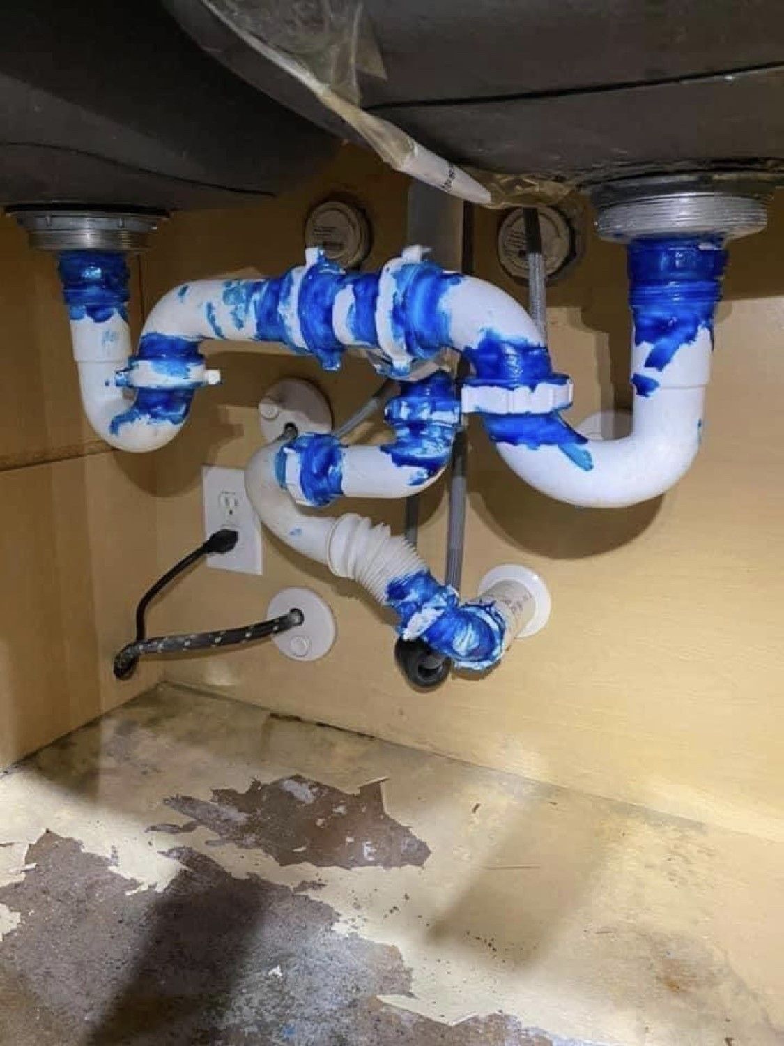 Blue and white wrapped plumbing pipes under a sink, with a wet floor below.