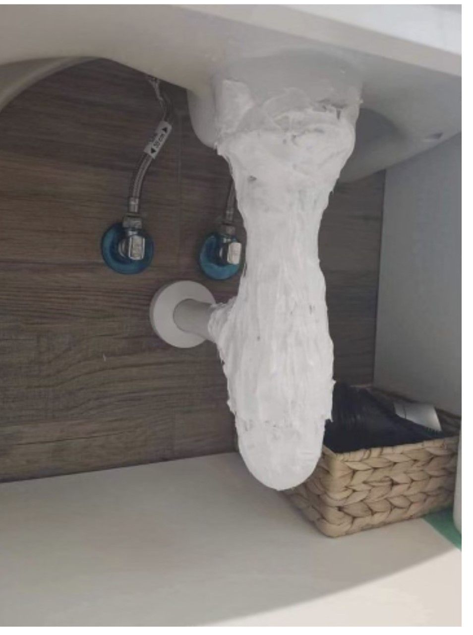 White insulation wrapped around a bathroom sink drainpipe and under the sink in a wooden cabinet.
