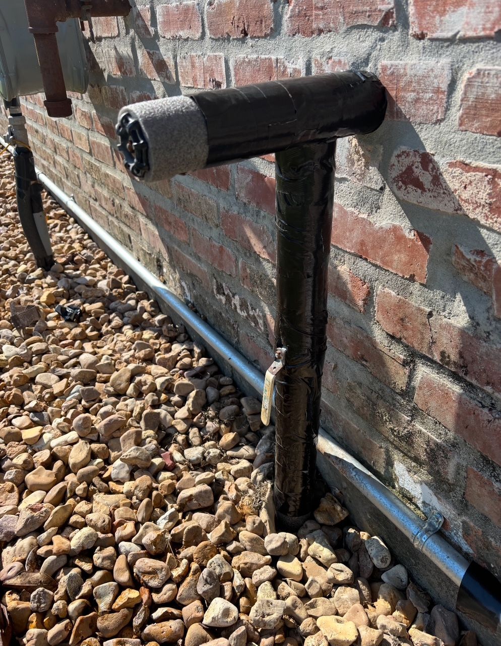 Black pipe against a brick wall, covered in tape, with gravel below.