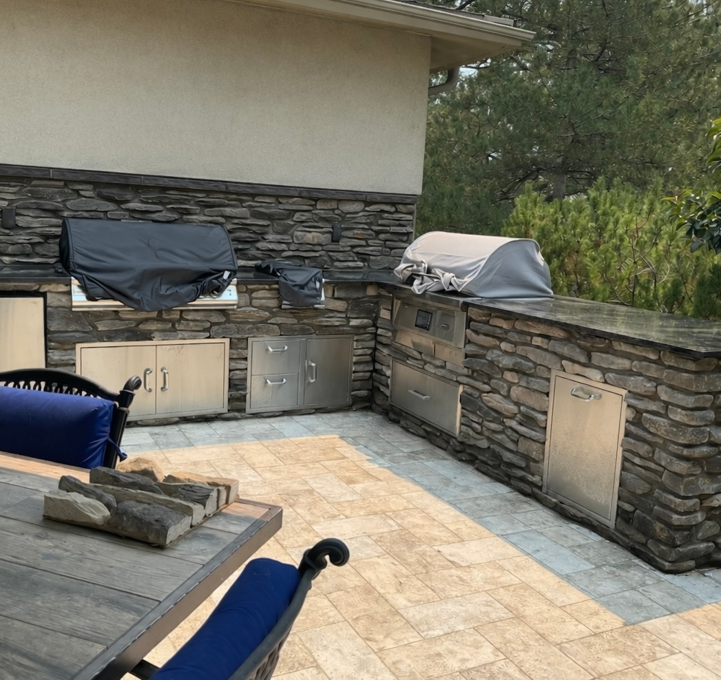 Outdoor kitchen with stone walls, stainless steel appliances, and a grill.