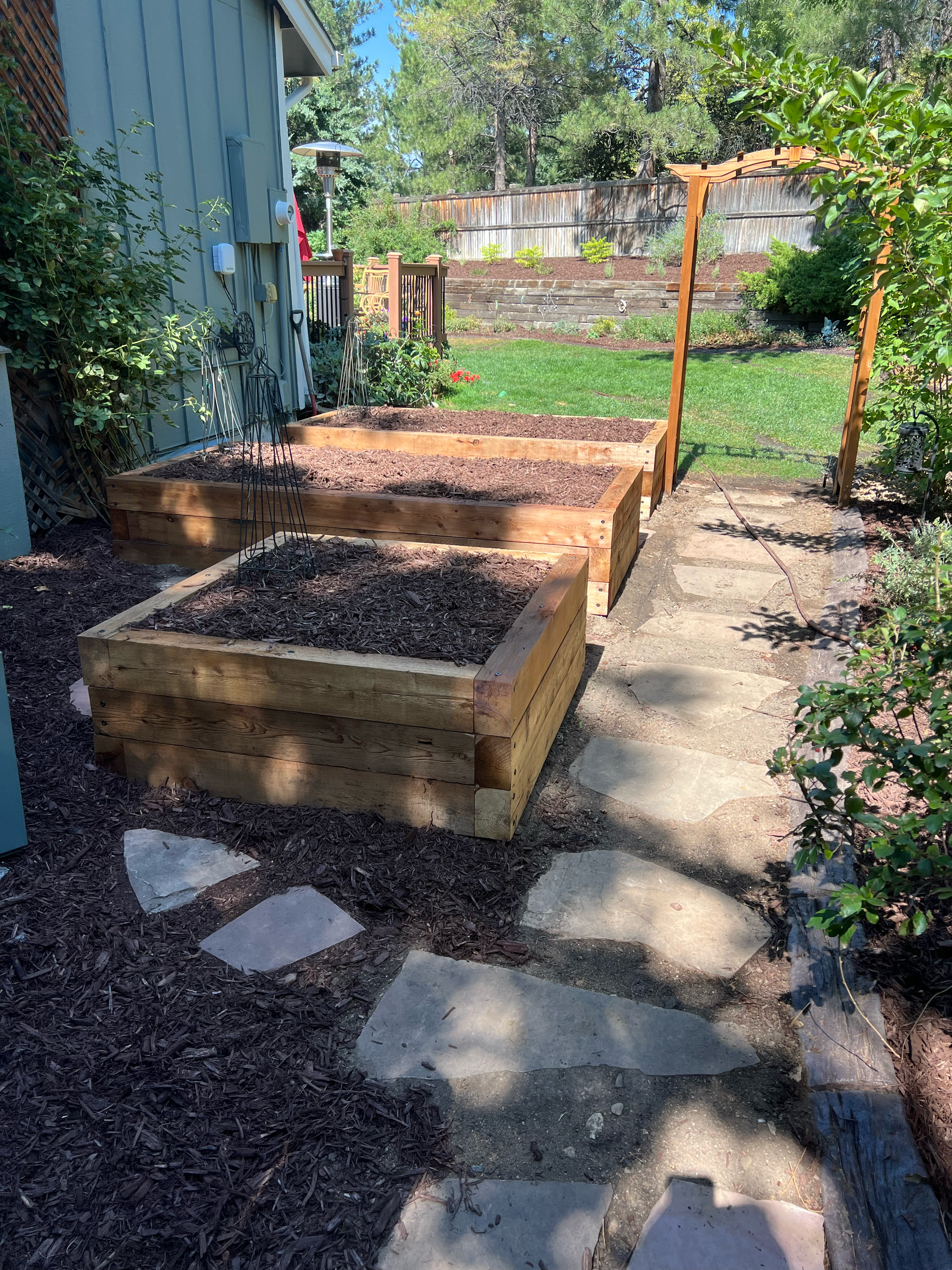 Two wooden raised garden beds with dark mulch, pathway, and wooden arch.
