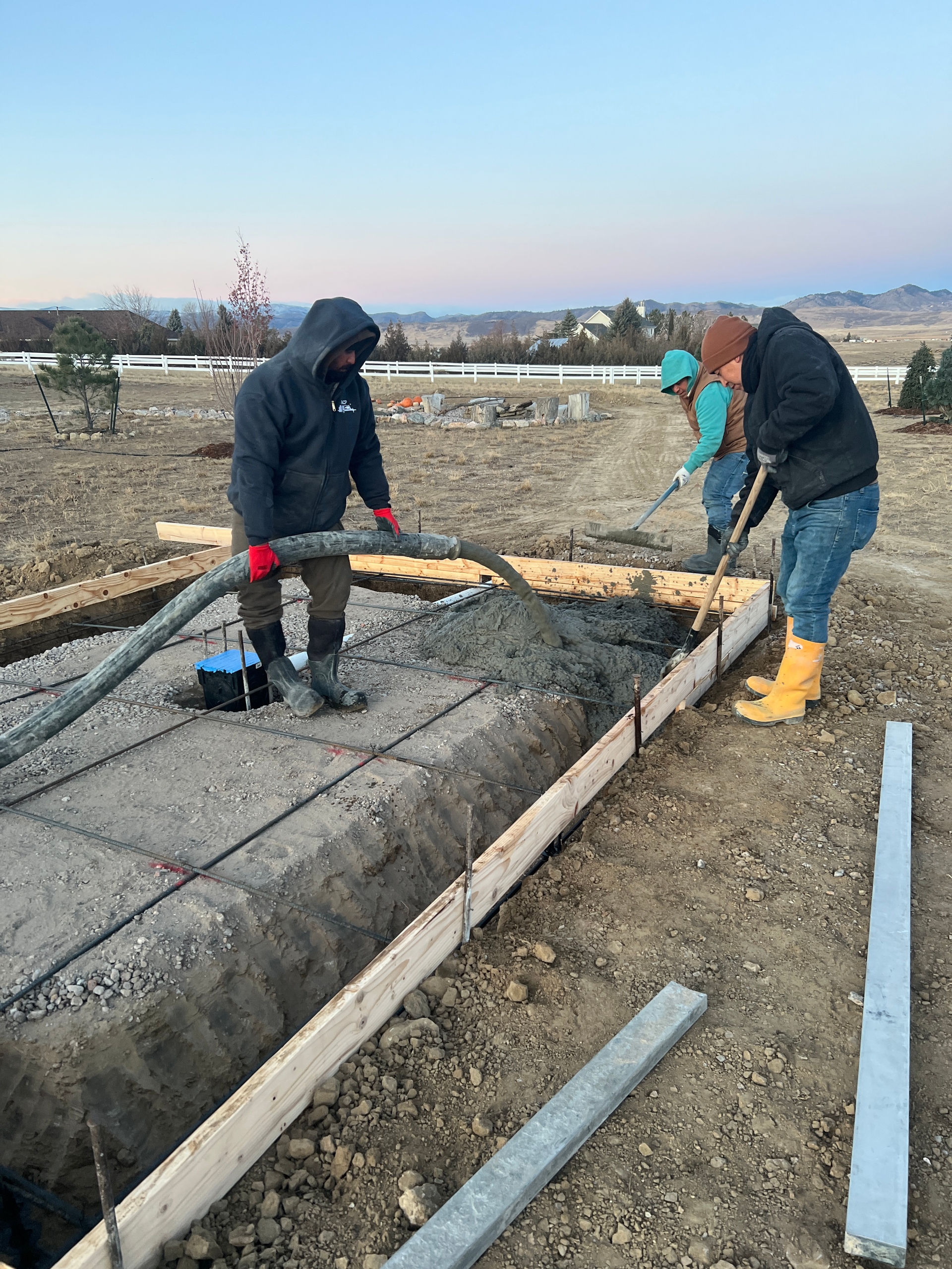 Construction workers pouring and leveling concrete into a form. Evening light; outdoors.