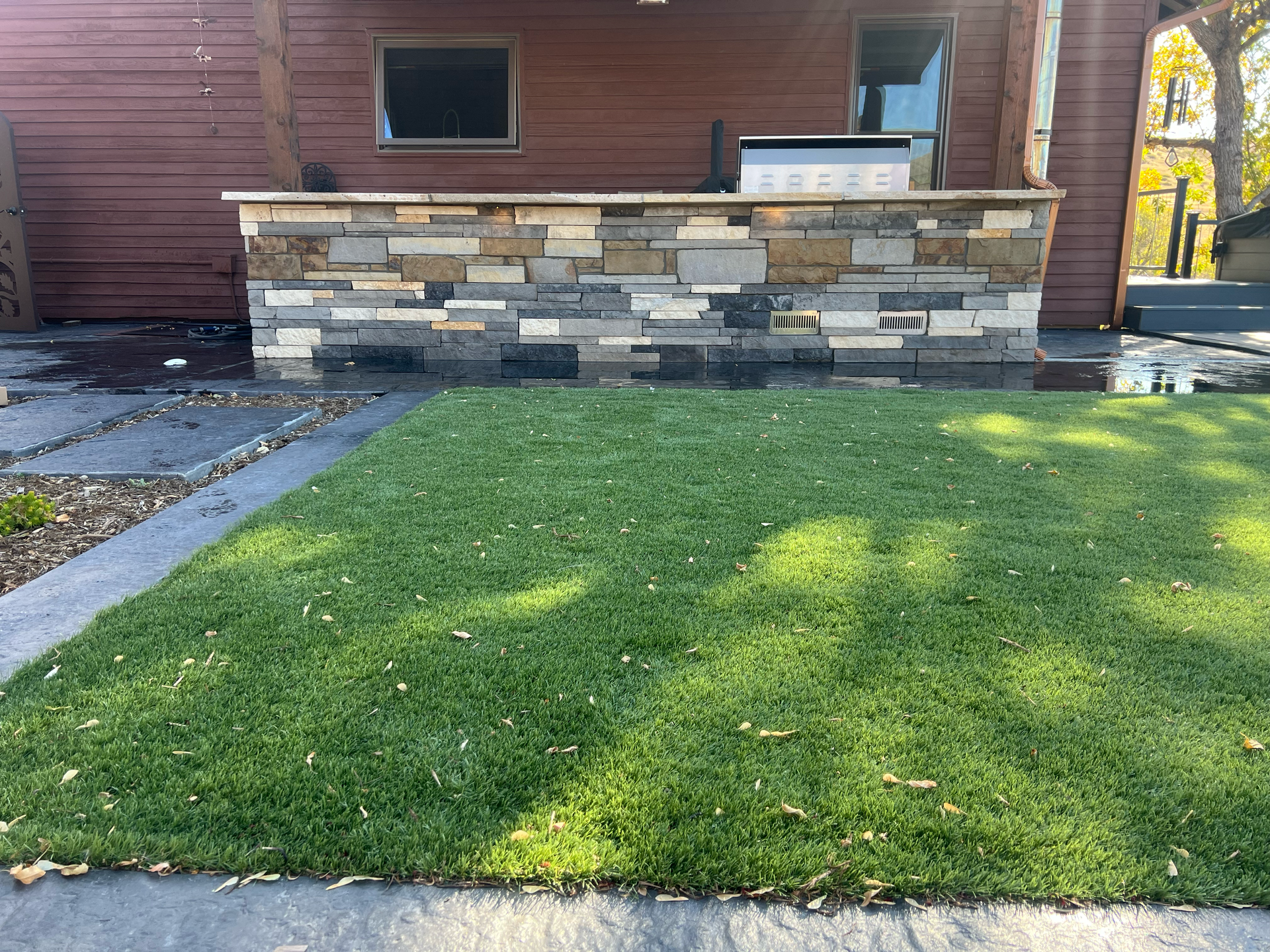 Stone-faced outdoor kitchen counter with built-in grill, next to a patch of green grass.