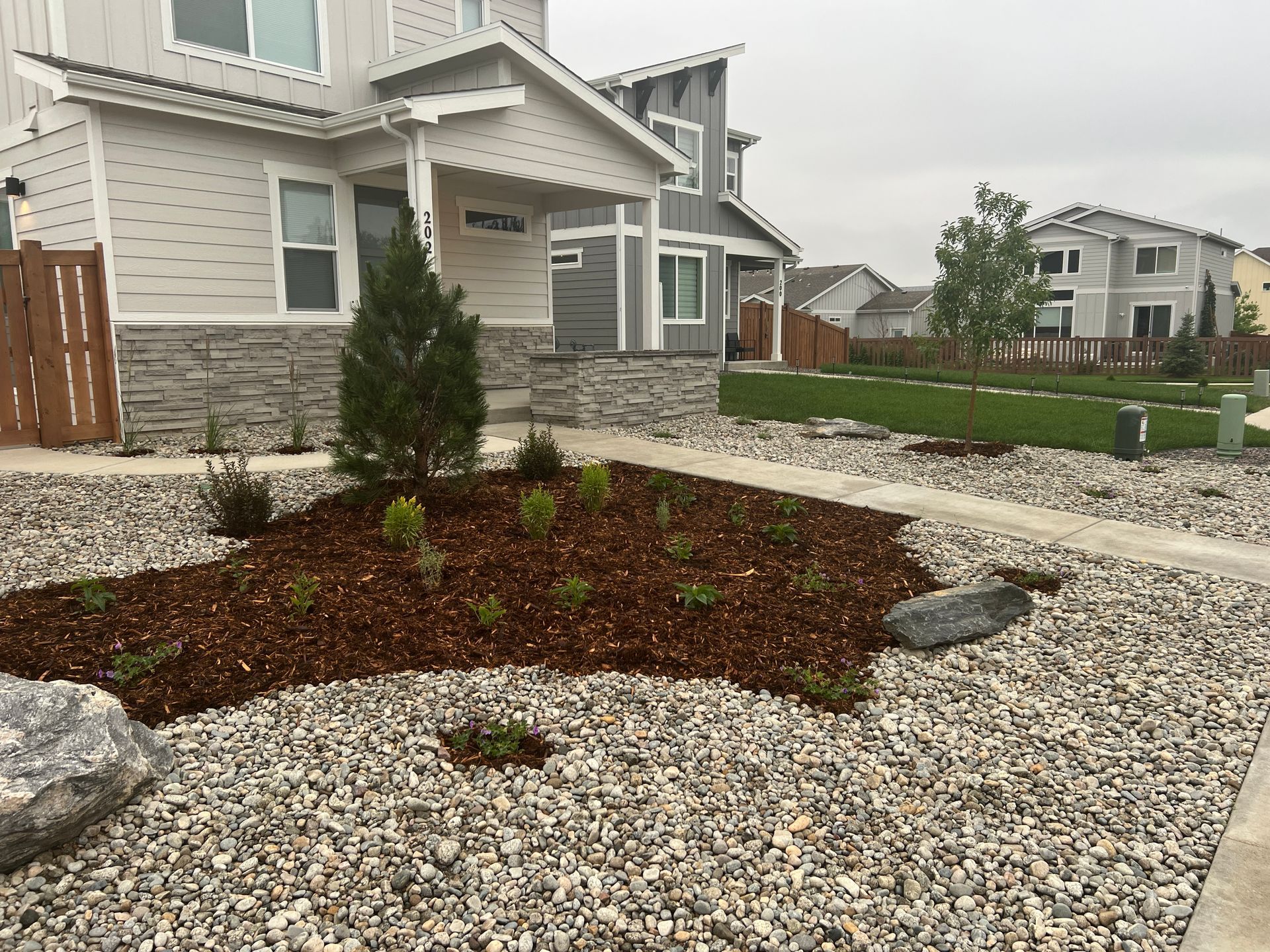 Front yard landscaping with gravel, mulch, and small plants in front of a modern house.