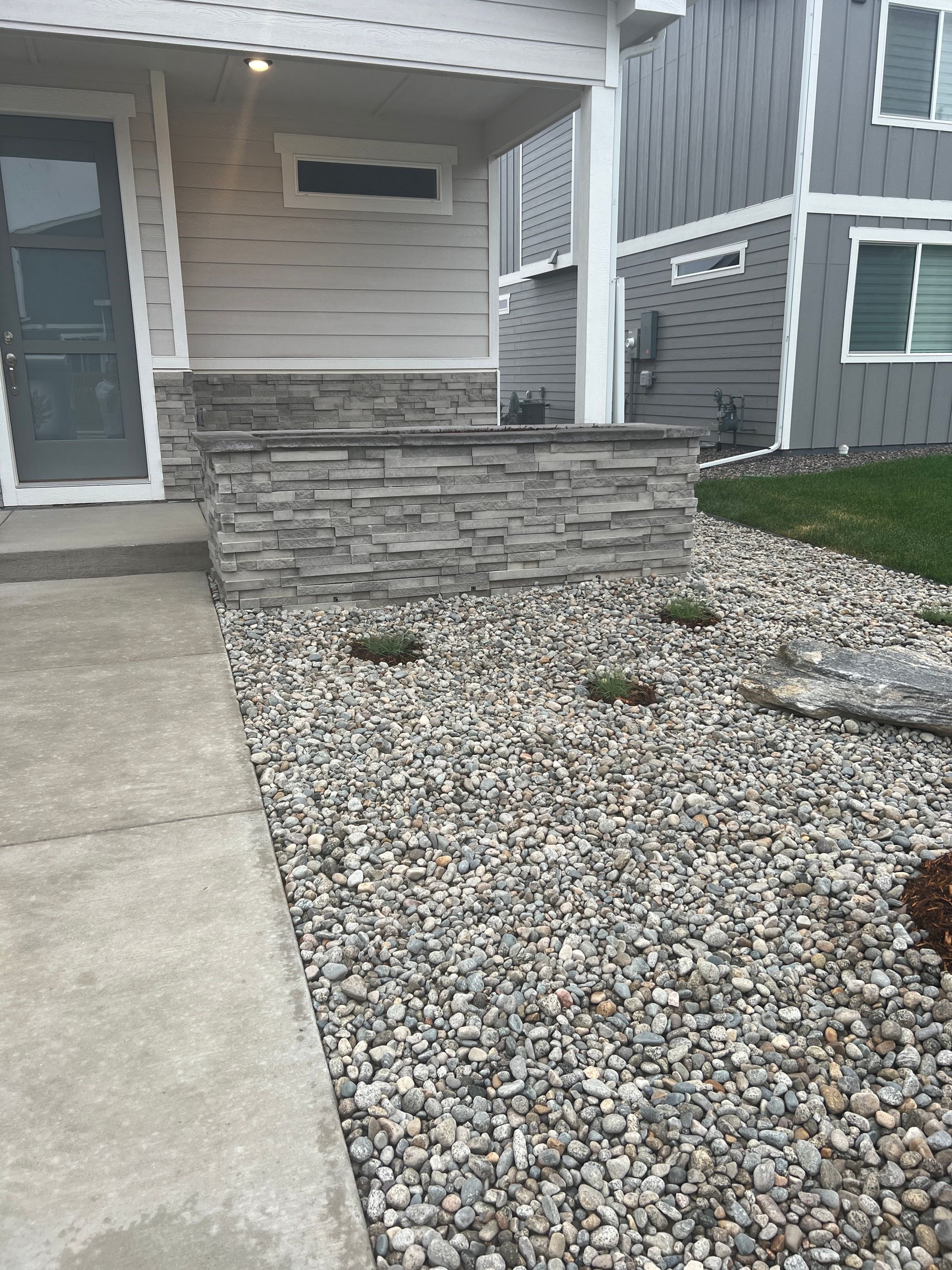 Gray stone veneer facade on a house with a rock landscape and concrete walkway.