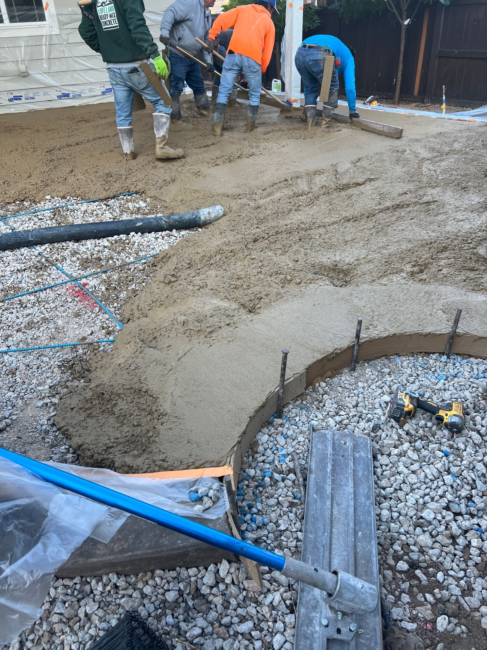 Construction workers pouring and smoothing concrete for a curved patio in an outdoor setting.