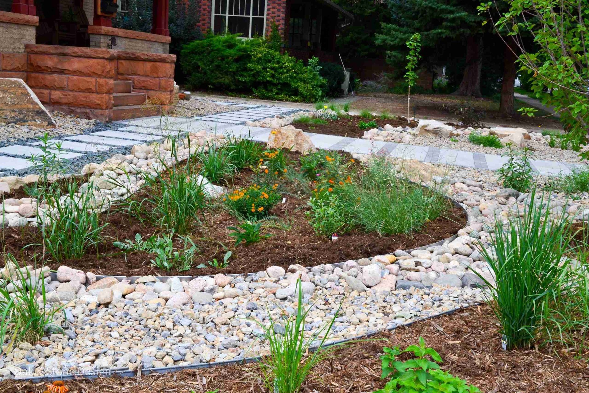 Landscaped front yard with a stone path, rock bed, and green plants.