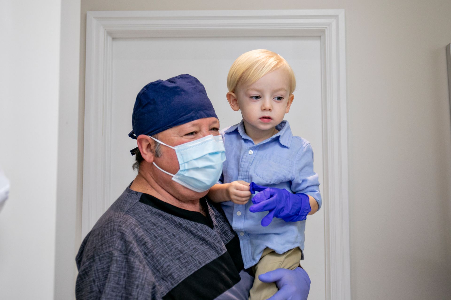 A man wearing a mask and gloves is holding a little boy.