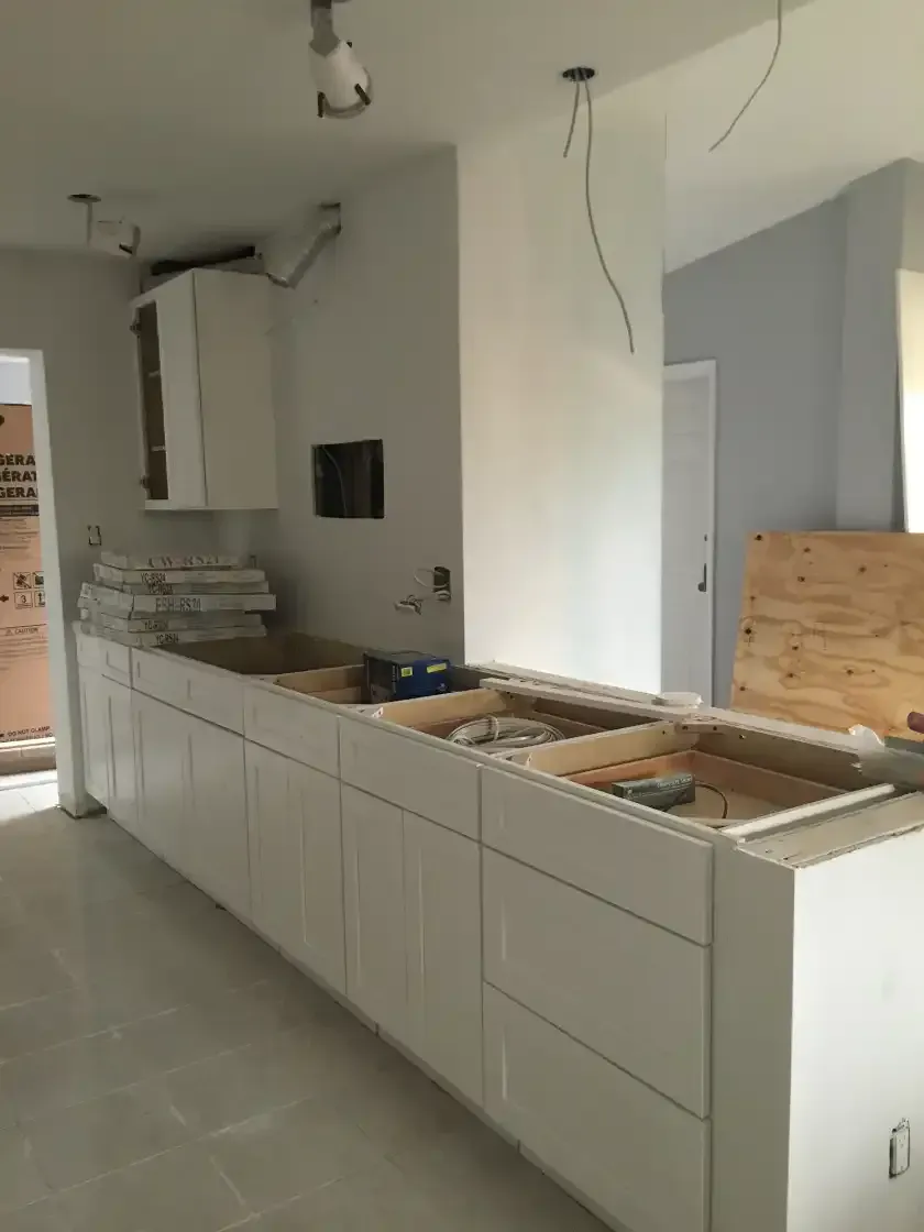 A kitchen under construction with white cabinets and wooden counter tops.