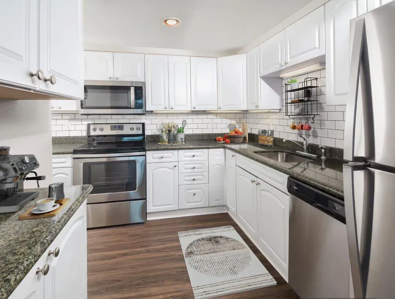White kitchen with stainless steel appliances, granite countertops, and hardwood floor.