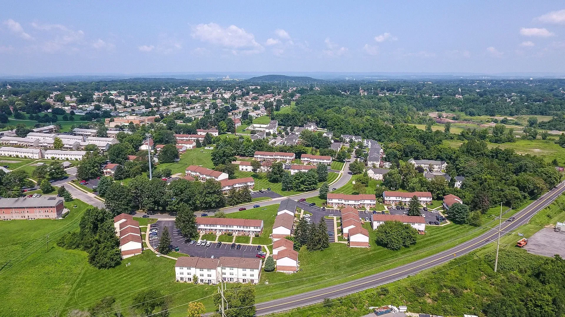 Aerial view of a residential area with buildings surrounded by green trees and grass, on a sunny day.