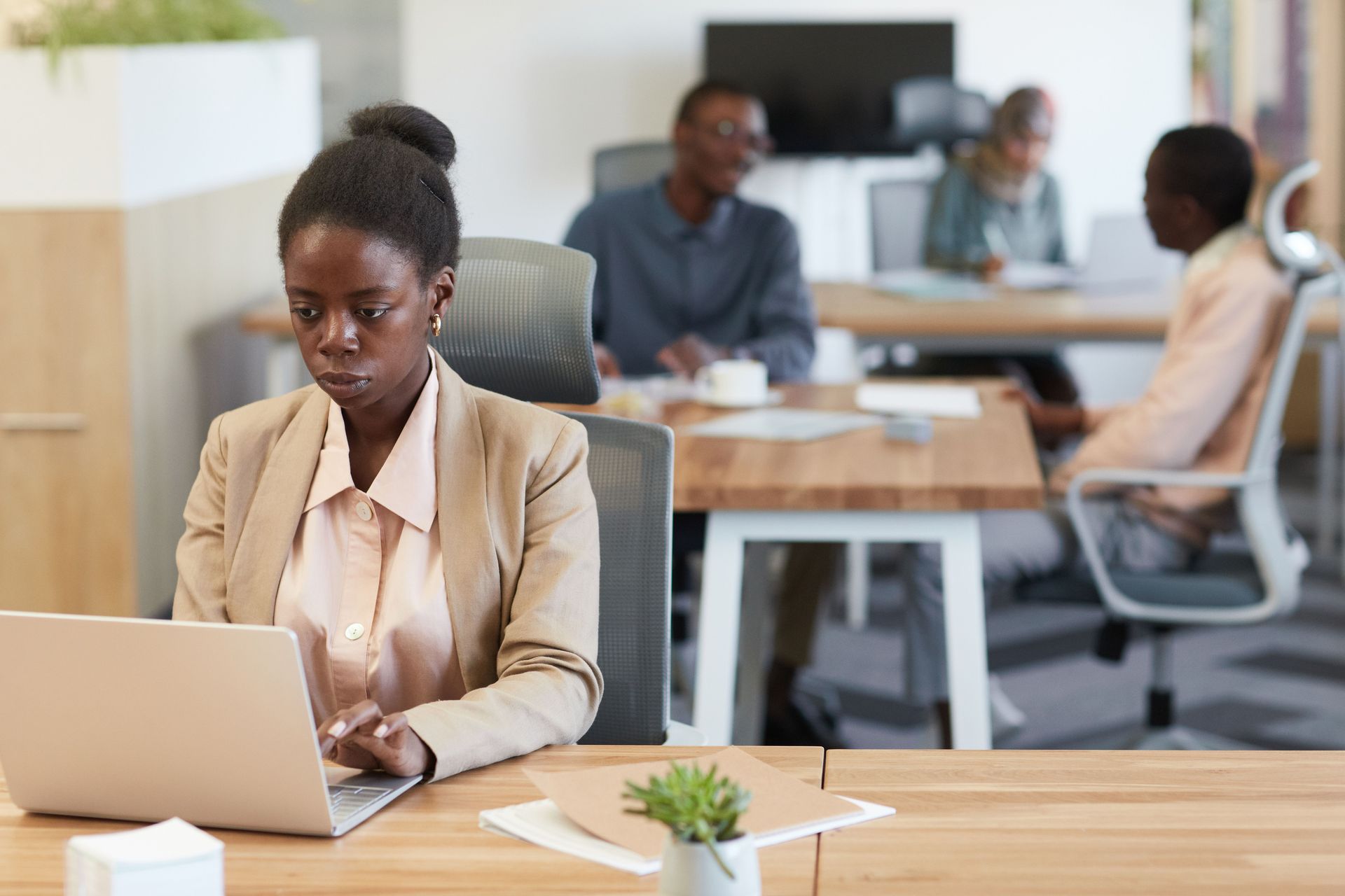 Woman working on a laptop in a modern office with colleagues in the background
