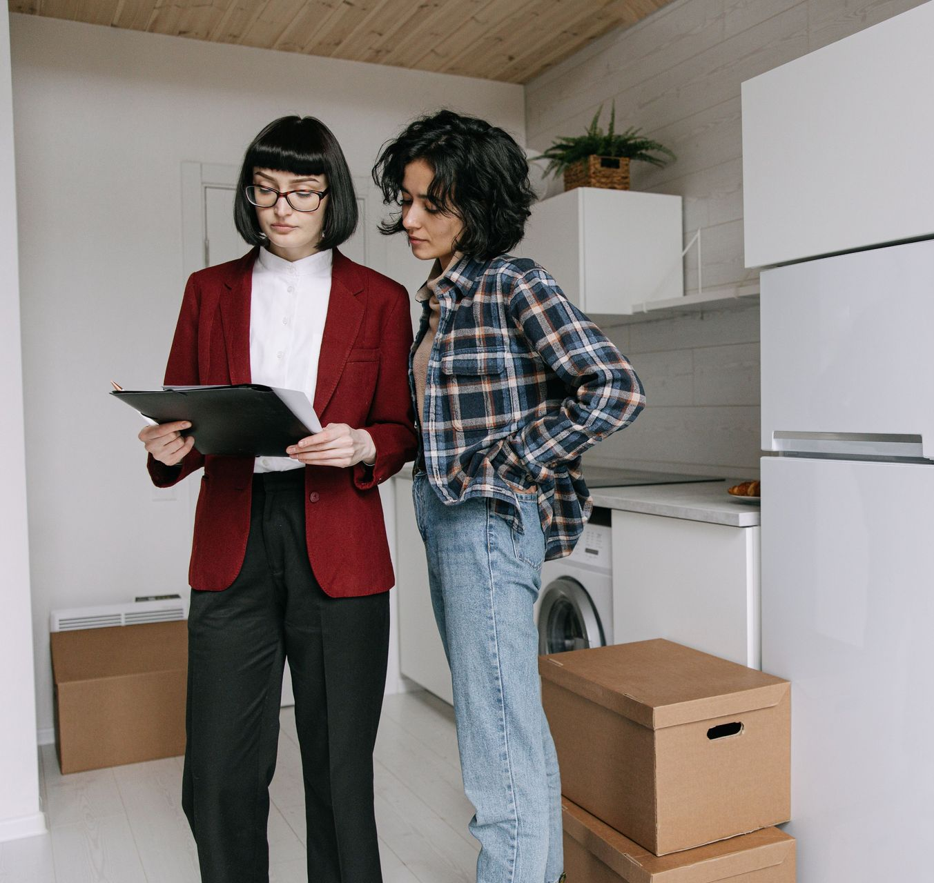 Two people reviewing a tablet in a bright kitchen with moving boxes nearby.