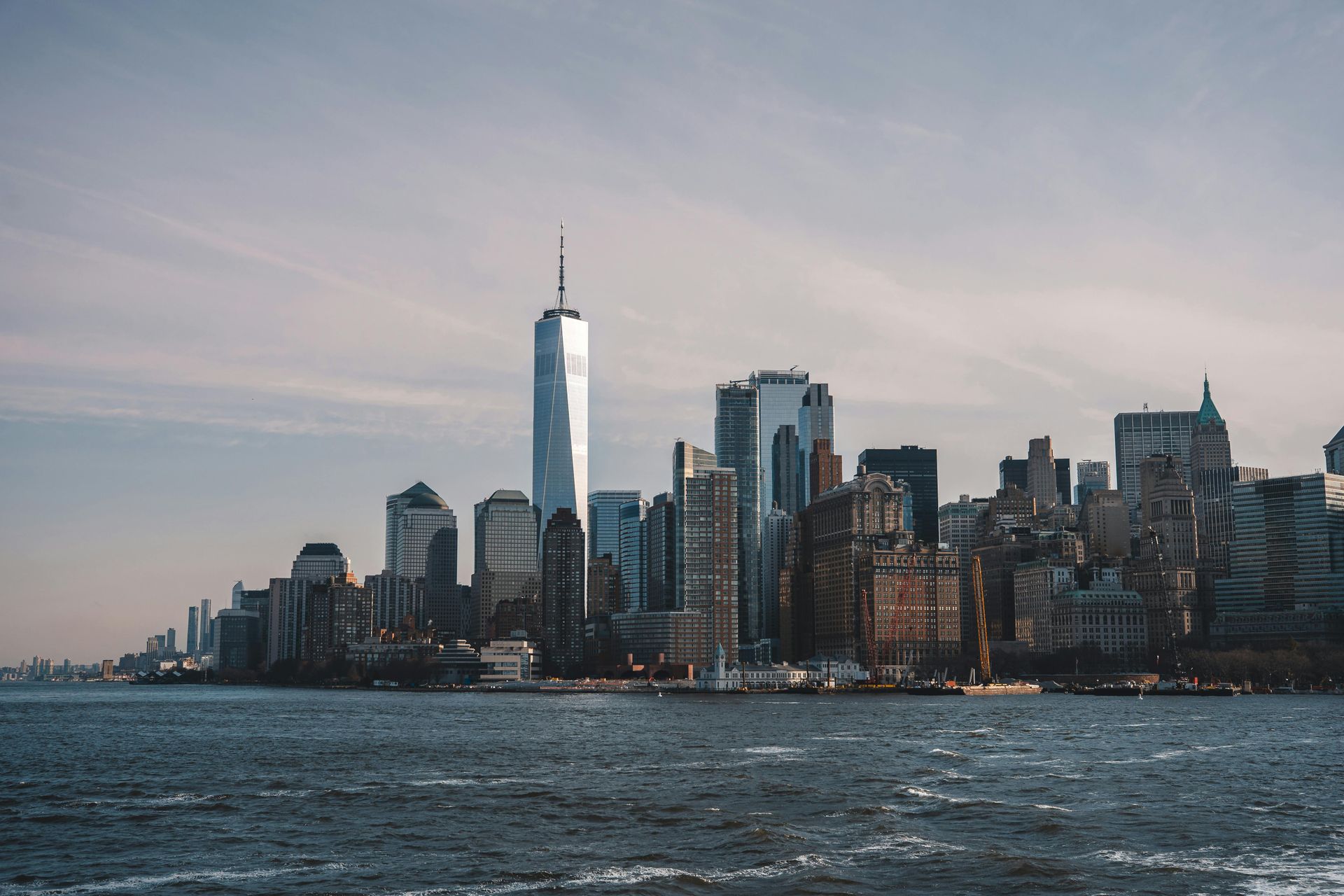 NYC skyline with One World Trade Center, seen from the water on a slightly overcast day.