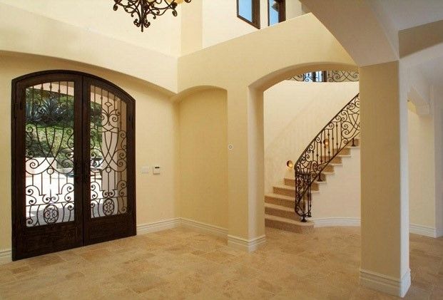 Elegant beige foyer with arched entryways, ornate double doors, and a curved staircase.