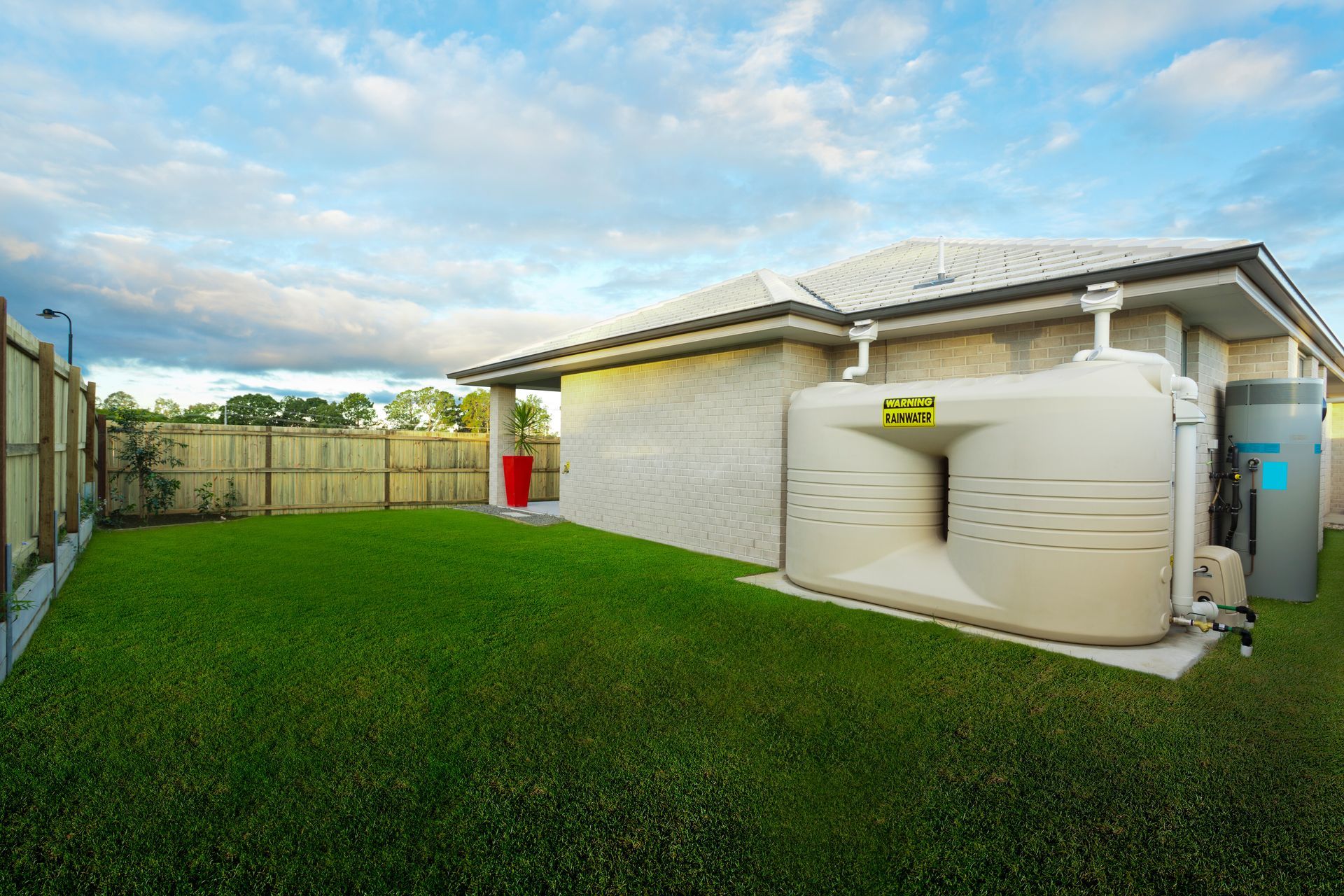 Backyard with green lawn, beige house, fence, and large white water tanks beside the wall