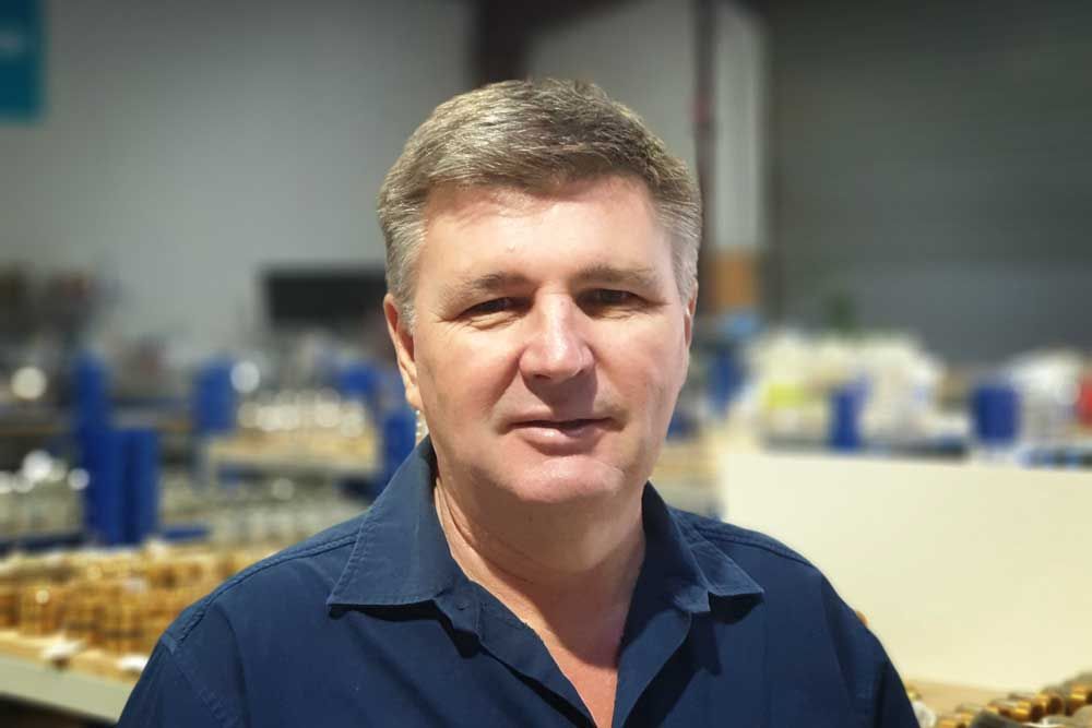 Man standing in a blue shirt in an industrial workshop with blurred machinery in the background
