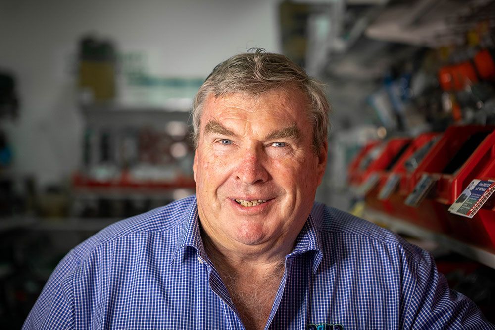 Man in a blue checkered shirt smiling in a workshop with red equipment in the background