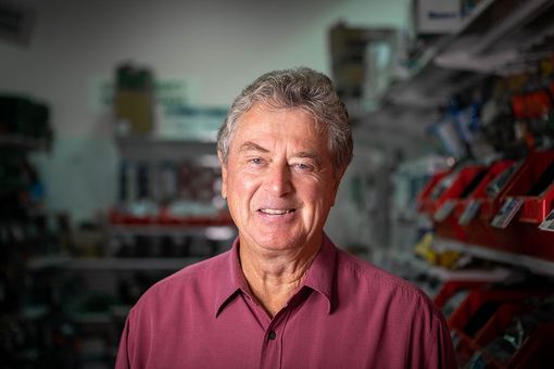 Smiling man in a red shirt standing in a store aisle with blurred tools in the background