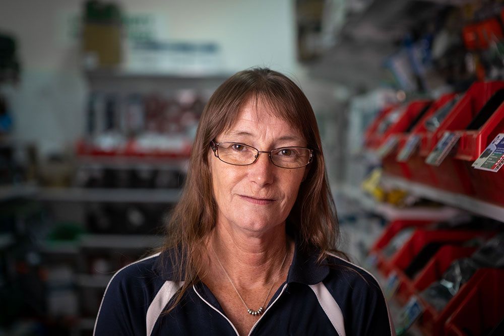 Woman with glasses standing in a store aisle, surrounded by shelves of red and black products.