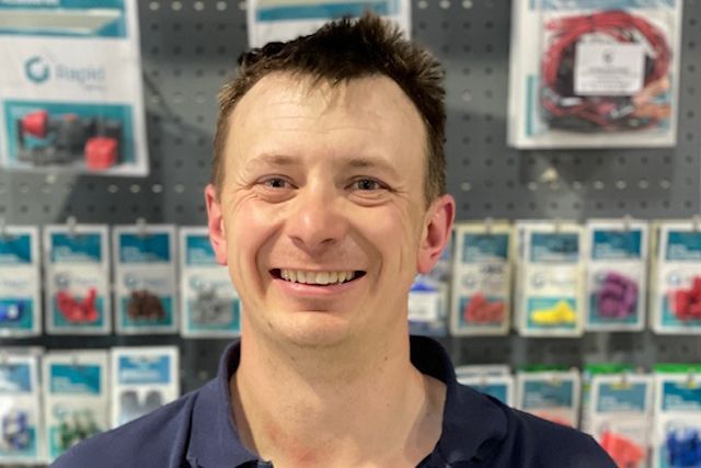 Smiling man in a navy shirt standing in front of a wall of packaged products