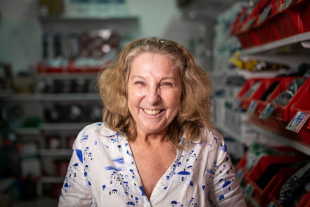 Smiling woman in a white floral blouse standing in a store aisle with red shelves in the background