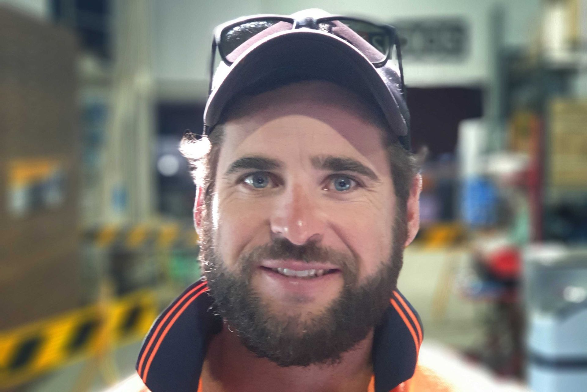 Smiling bearded man in a cap standing in an industrial warehouse setting