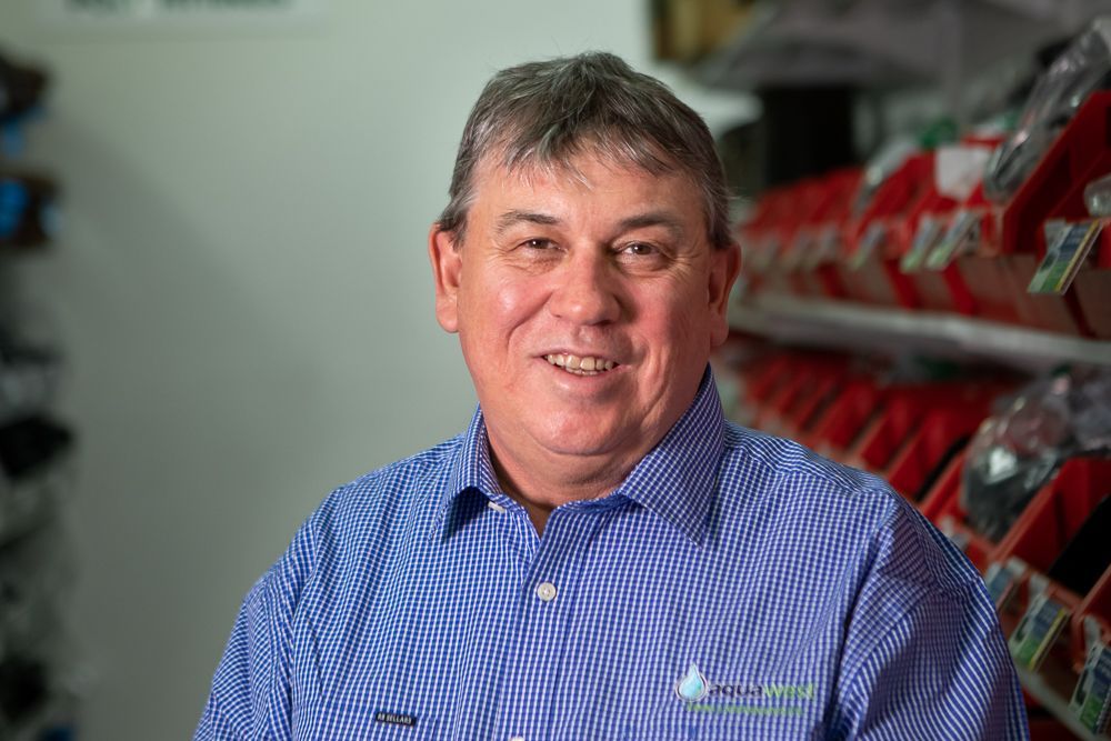 Man in a blue checkered shirt smiling in a store aisle with red products in the background