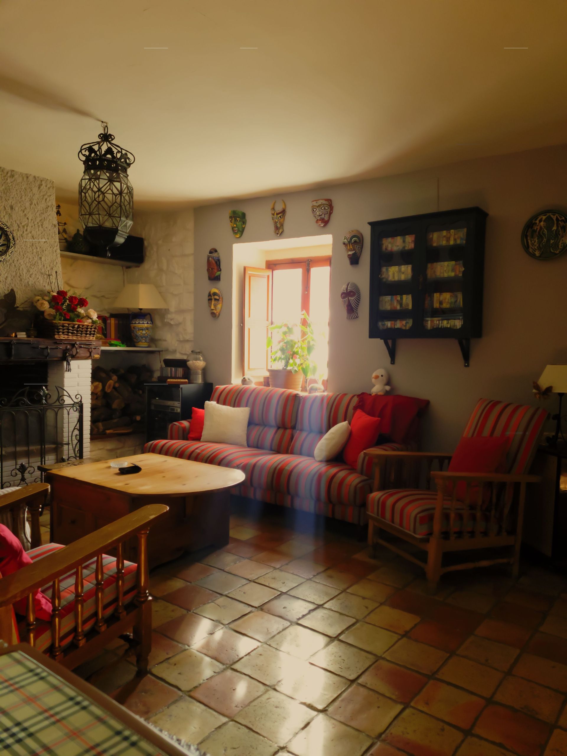 Cozy living room with striped sofa, fireplace, wooden chairs, tiled floor, and warm light