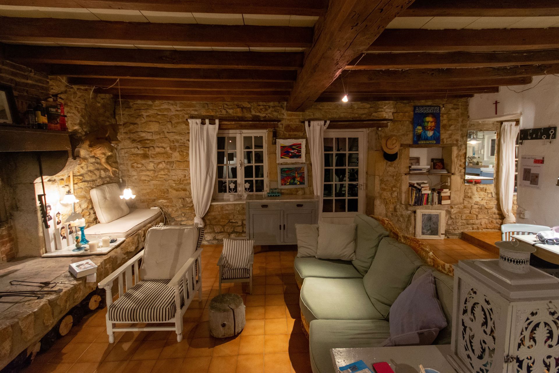 Cozy rustic living room with exposed beams, stone walls, sofa, bench, and warm lamplight