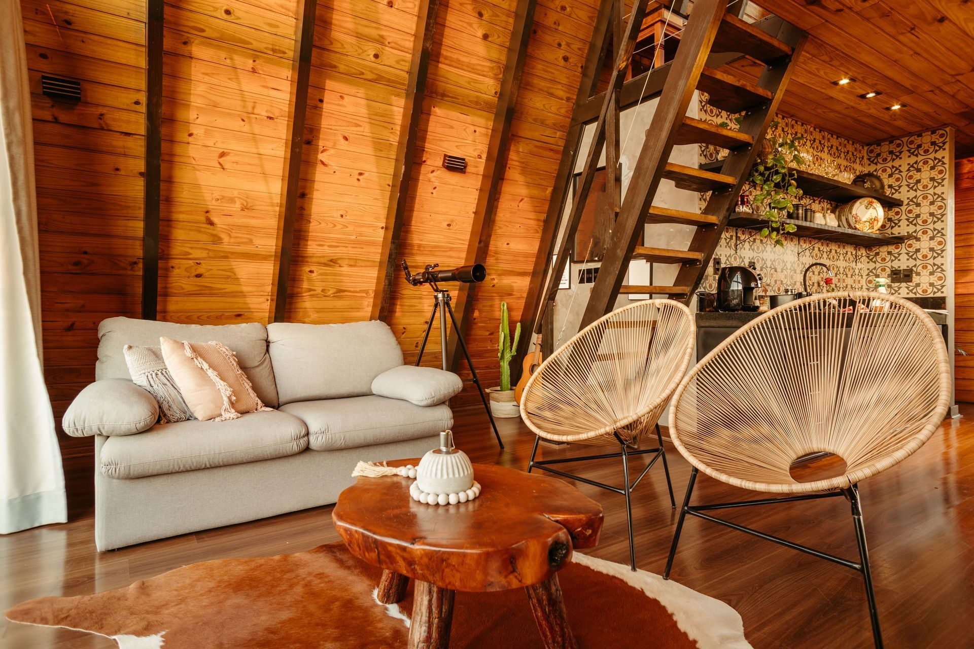 Cozy loft living room with a beige sofa, wicker chairs, wooden table, and slanted wood-paneled ceiling