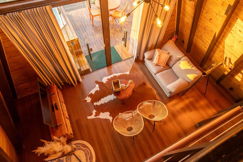 Cozy wooden loft with sofa, round tables, and warm string lights overlooking a small balcony